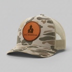 Camouflage trucker hat with a brown leather patch featuring 'Real Momentum' logo on a white background.