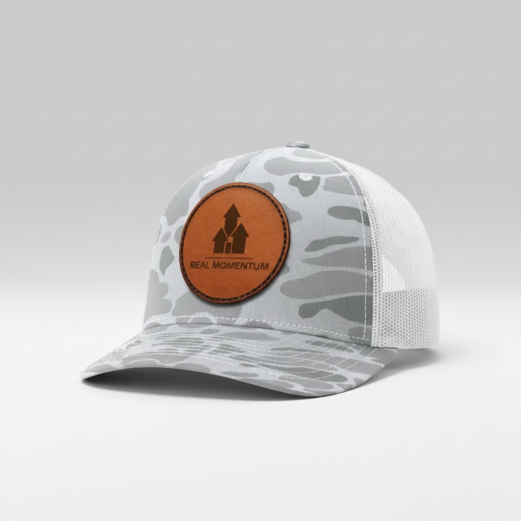 Camouflage-patterned cap with a brown leather patch featuring 'Real Momentum' logo on a white background