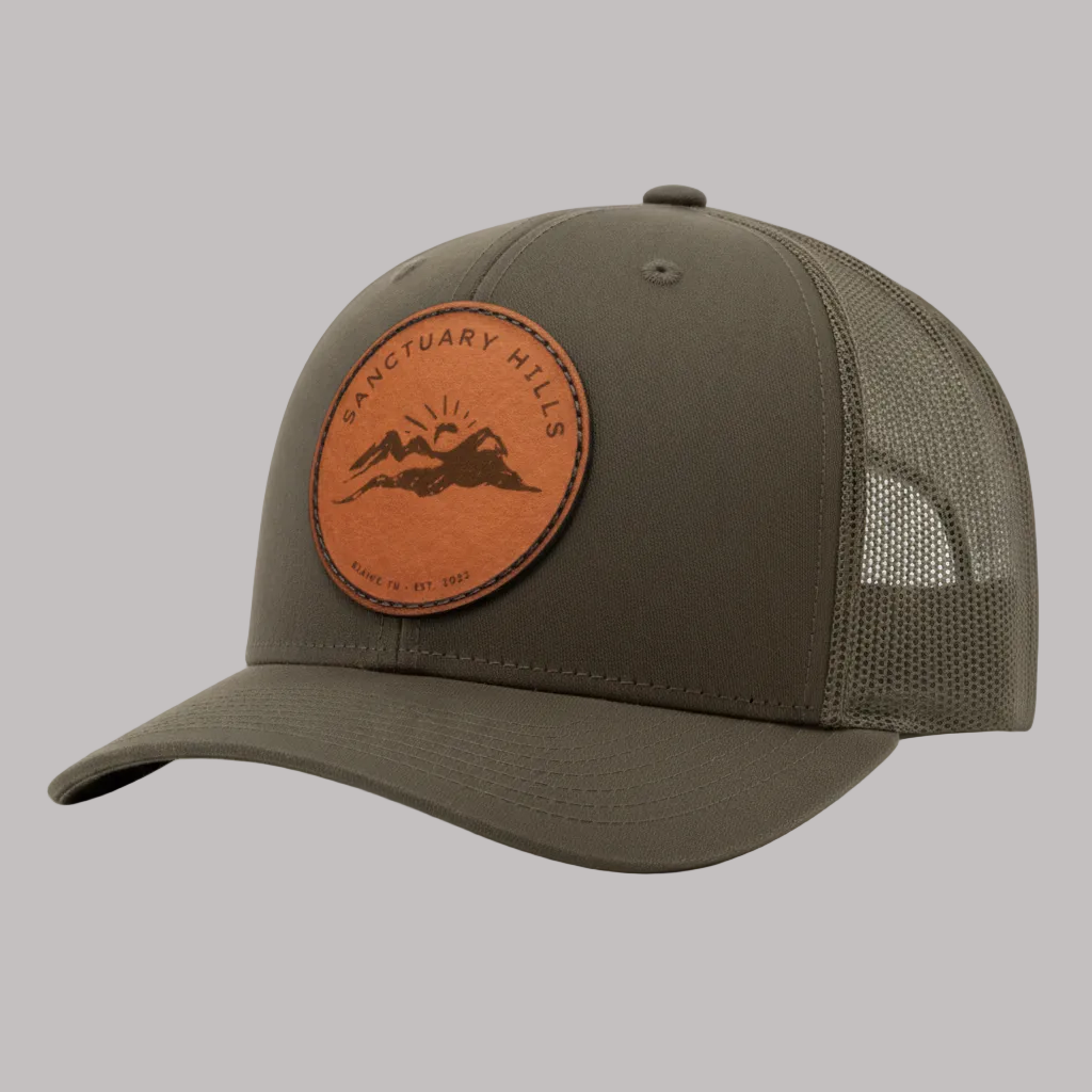 Green cap with brown leather patch featuring a mountain design on a white background